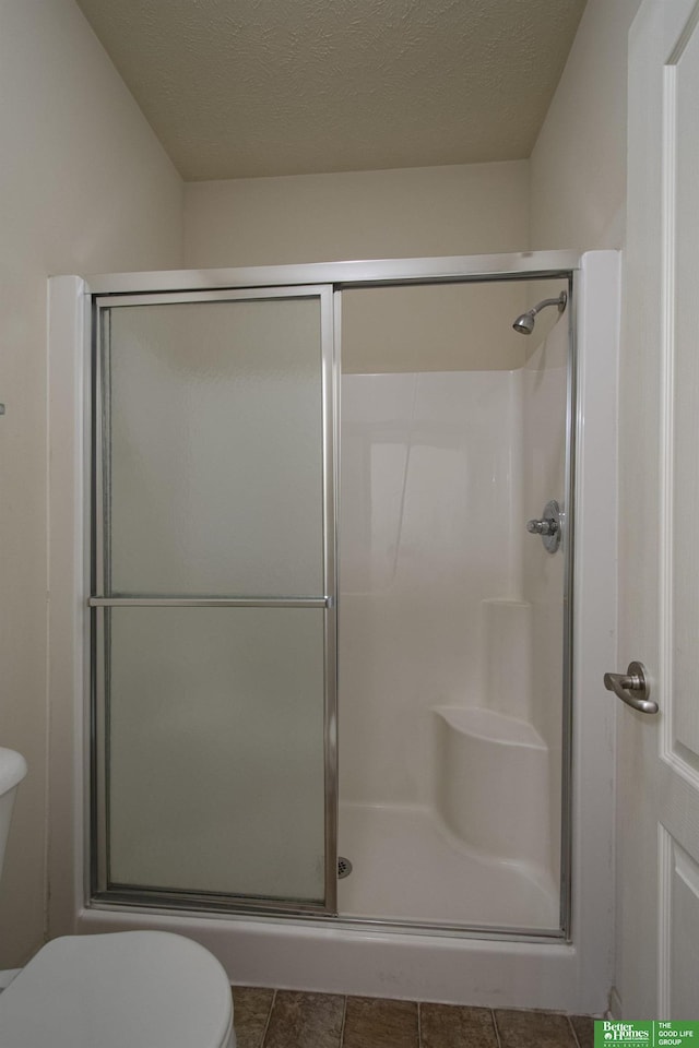 bathroom featuring toilet, a textured ceiling, and an enclosed shower