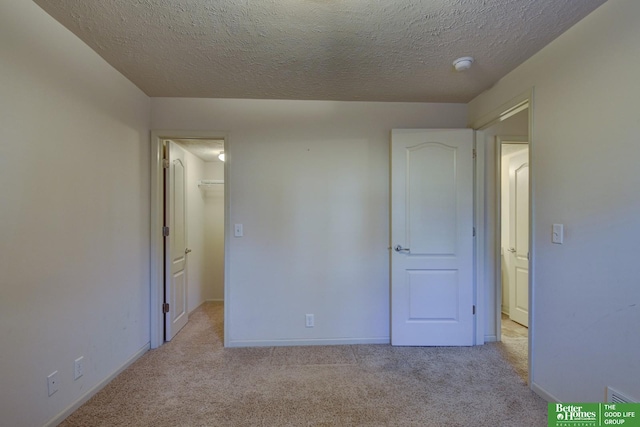 unfurnished bedroom with light carpet, a walk in closet, a closet, and a textured ceiling