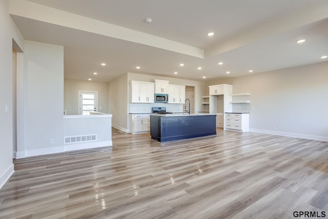 kitchen with white cabinets, sink, light hardwood / wood-style flooring, stainless steel appliances, and a center island with sink