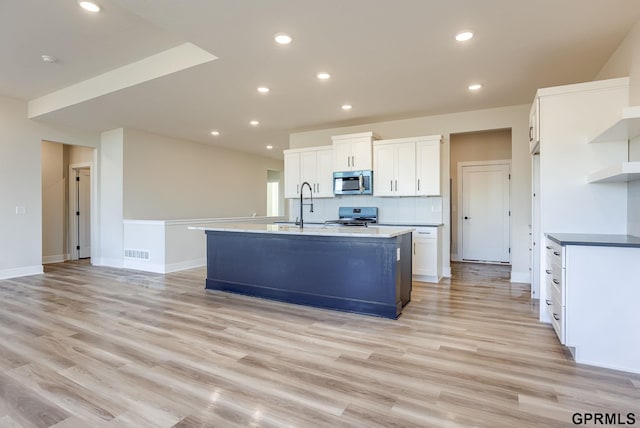 kitchen with an island with sink, white cabinets, light hardwood / wood-style flooring, and appliances with stainless steel finishes