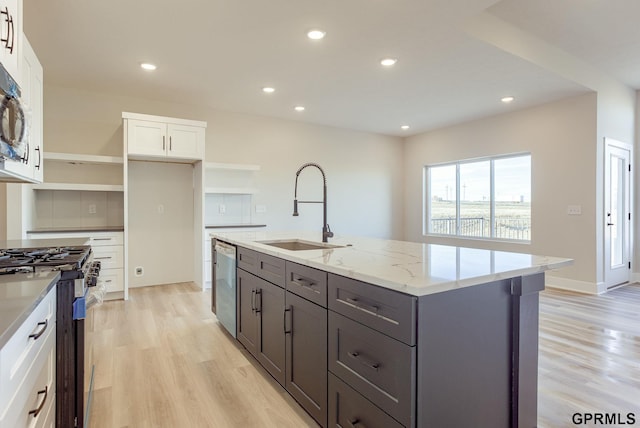 kitchen featuring white cabinets, sink, stainless steel appliances, light stone counters, and a center island with sink