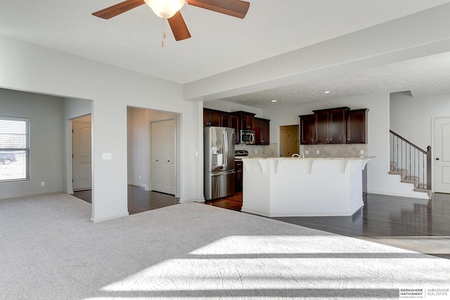 kitchen featuring appliances with stainless steel finishes, tasteful backsplash, a breakfast bar, dark carpet, and a center island with sink