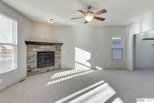 unfurnished living room featuring ceiling fan, carpet, and a stone fireplace