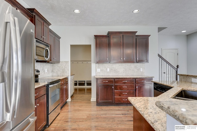 kitchen featuring light stone countertops, a textured ceiling, appliances with stainless steel finishes, and light hardwood / wood-style flooring