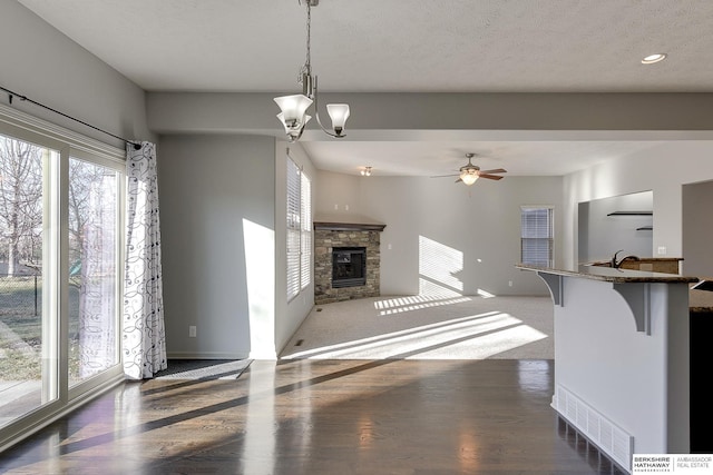 unfurnished living room with a textured ceiling, ceiling fan with notable chandelier, a fireplace, and dark colored carpet