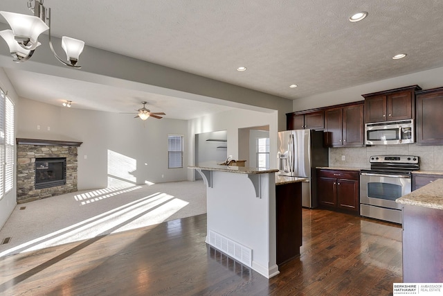 kitchen featuring tasteful backsplash, hanging light fixtures, a kitchen breakfast bar, a stone fireplace, and stainless steel appliances