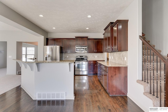 kitchen featuring stainless steel appliances, a kitchen bar, dark hardwood / wood-style floors, and light stone countertops