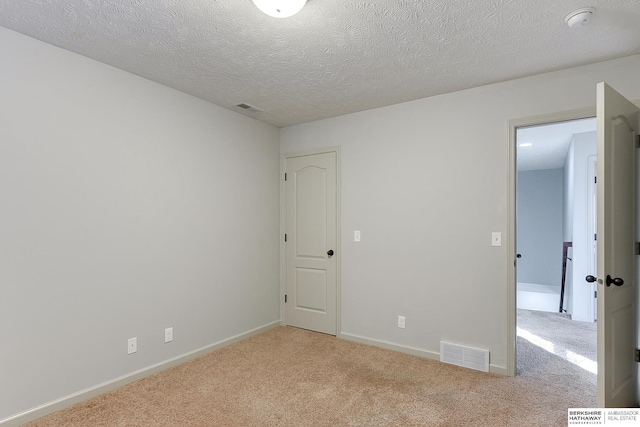 spare room featuring a textured ceiling and light colored carpet