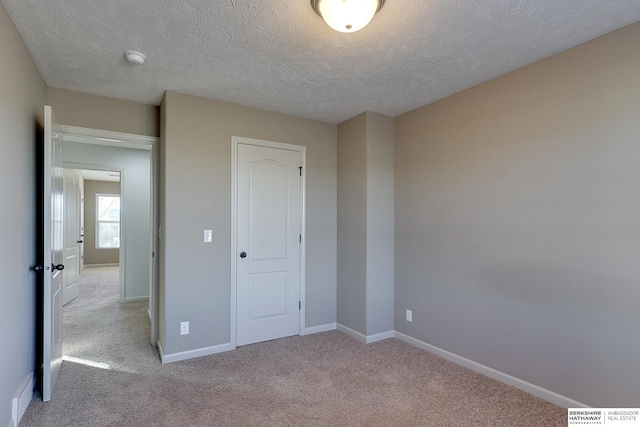 unfurnished bedroom featuring a textured ceiling, a closet, and light colored carpet