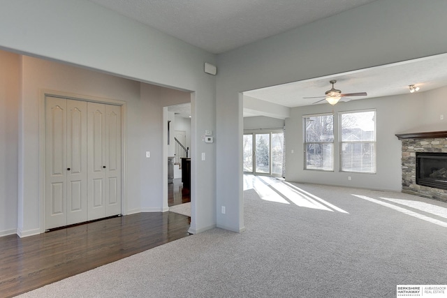 unfurnished living room with ceiling fan, a fireplace, a textured ceiling, and dark colored carpet