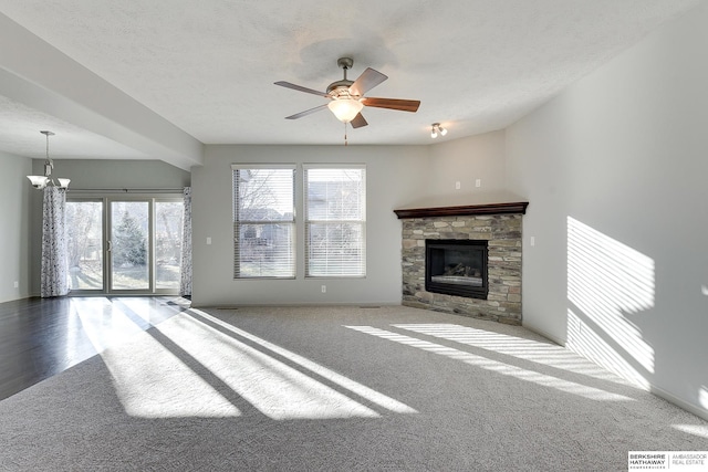 unfurnished living room featuring ceiling fan with notable chandelier, a textured ceiling, a stone fireplace, and a healthy amount of sunlight