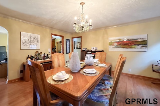 dining space with crown molding, wood-type flooring, and a notable chandelier