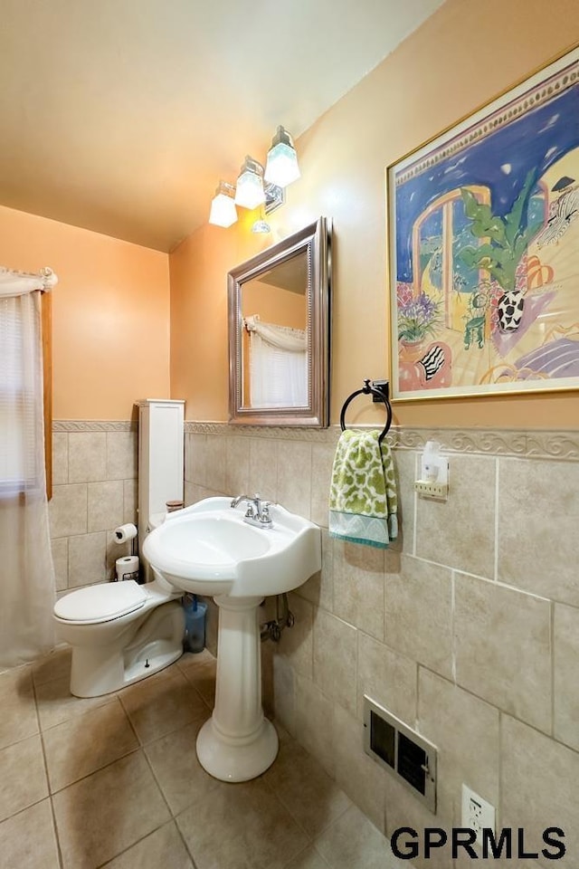 bathroom with toilet, sink, tile walls, and tile patterned floors