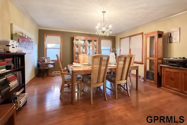 dining space featuring a notable chandelier, crown molding, a textured ceiling, and hardwood / wood-style flooring