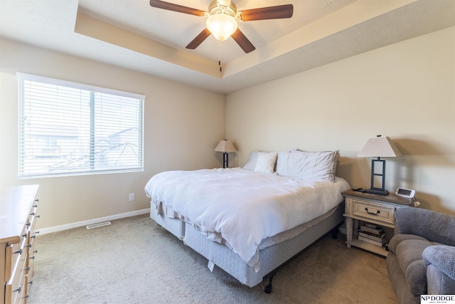 bedroom with ceiling fan, light colored carpet, and a raised ceiling