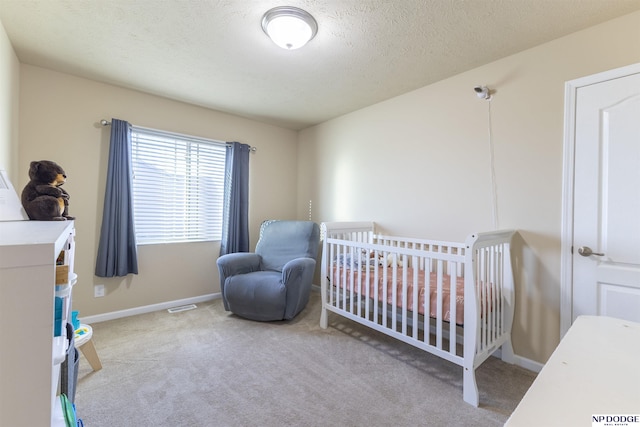 carpeted bedroom with a crib and a textured ceiling