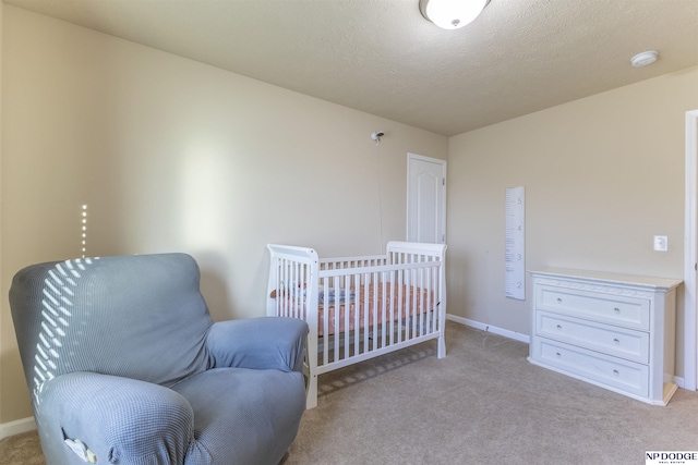 bedroom featuring a textured ceiling, light colored carpet, and a nursery area