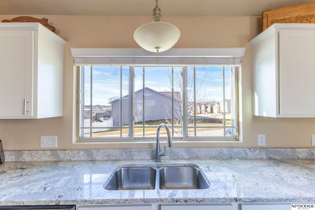 kitchen featuring light stone countertops, decorative light fixtures, white cabinets, and sink