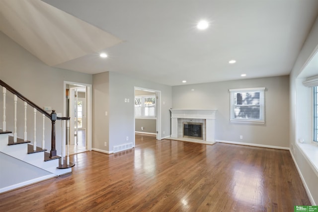 unfurnished living room featuring plenty of natural light, wood-type flooring, and a tiled fireplace