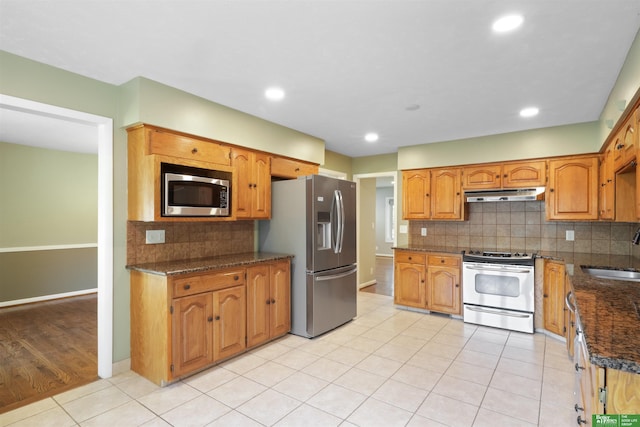 kitchen with light tile patterned floors, appliances with stainless steel finishes, tasteful backsplash, dark stone counters, and sink