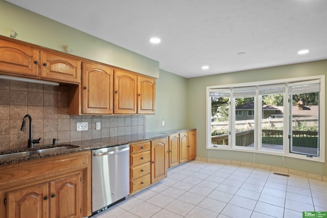 kitchen with dishwasher, dark stone counters, sink, backsplash, and light tile patterned floors