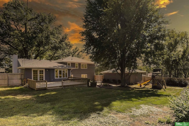 back house at dusk with a lawn, a deck, and a playground