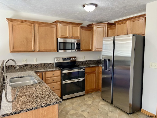 kitchen featuring a textured ceiling, stainless steel appliances, dark stone countertops, and sink