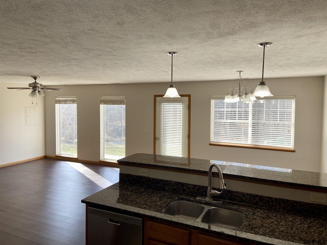 kitchen with stainless steel dishwasher, sink, hanging light fixtures, dark stone counters, and ceiling fan with notable chandelier