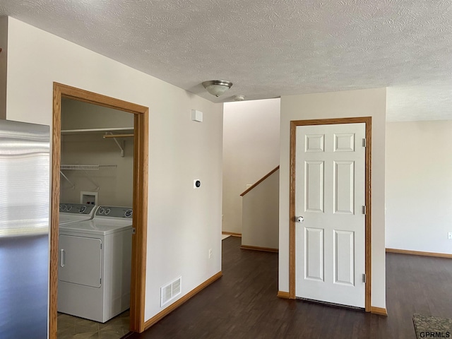 clothes washing area featuring dark wood-type flooring, washing machine and clothes dryer, and a textured ceiling