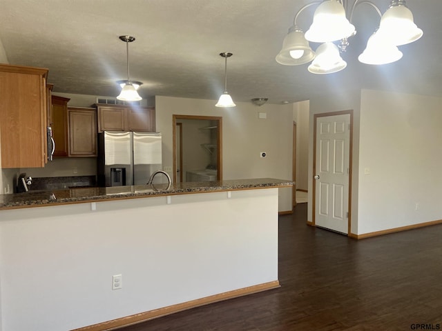 kitchen with dark stone countertops, pendant lighting, kitchen peninsula, dark wood-type flooring, and appliances with stainless steel finishes