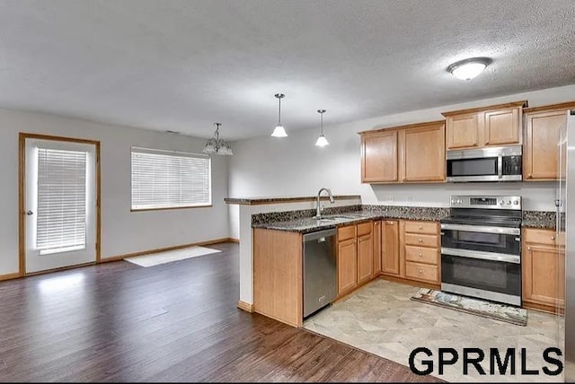 kitchen with decorative light fixtures, kitchen peninsula, stainless steel appliances, and dark stone countertops