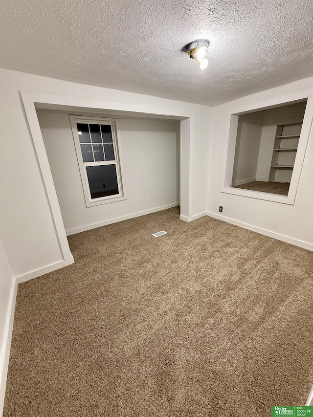 spare room with a textured ceiling, carpet flooring, and built in features