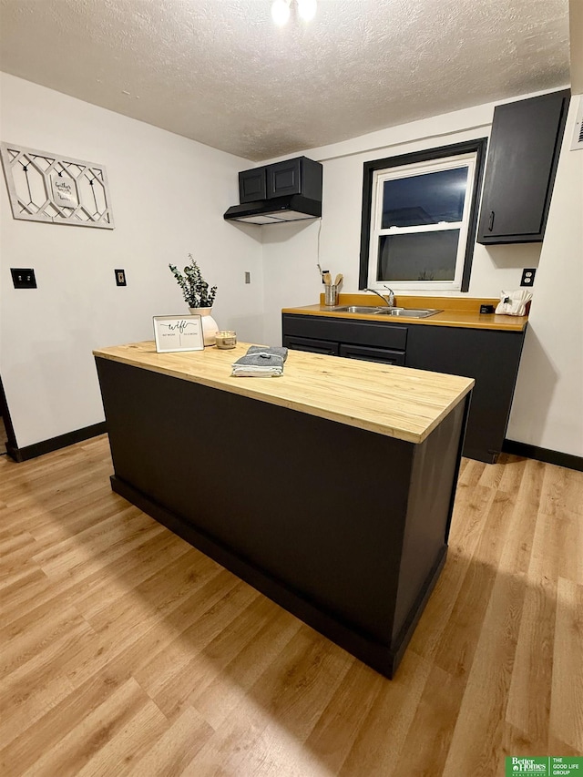 kitchen with a textured ceiling, light hardwood / wood-style flooring, butcher block countertops, and sink