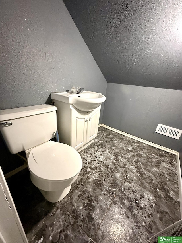 bathroom with toilet, vanity, vaulted ceiling, and a textured ceiling