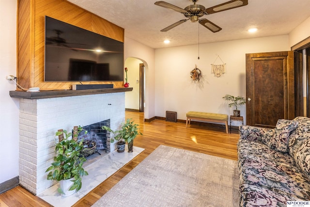 living room featuring a textured ceiling, a fireplace, light hardwood / wood-style floors, and ceiling fan