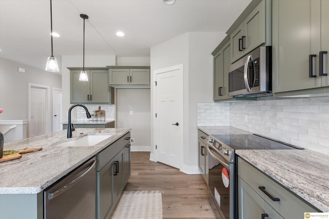 kitchen with pendant lighting, sink, light hardwood / wood-style flooring, light stone countertops, and stainless steel appliances