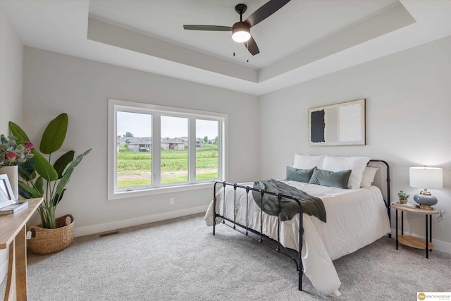 carpeted bedroom featuring ceiling fan and a tray ceiling