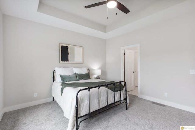 carpeted bedroom with ceiling fan and a tray ceiling