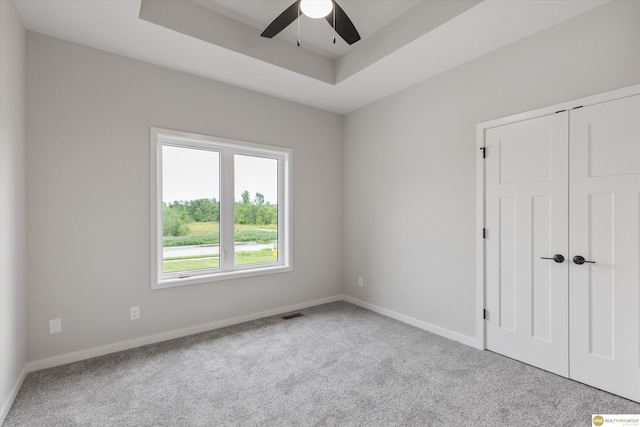 carpeted empty room featuring ceiling fan and a tray ceiling