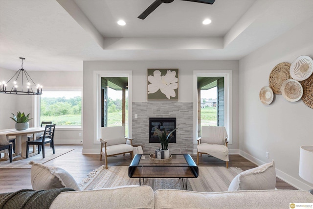 living room featuring ceiling fan with notable chandelier, a fireplace, hardwood / wood-style floors, and a tray ceiling