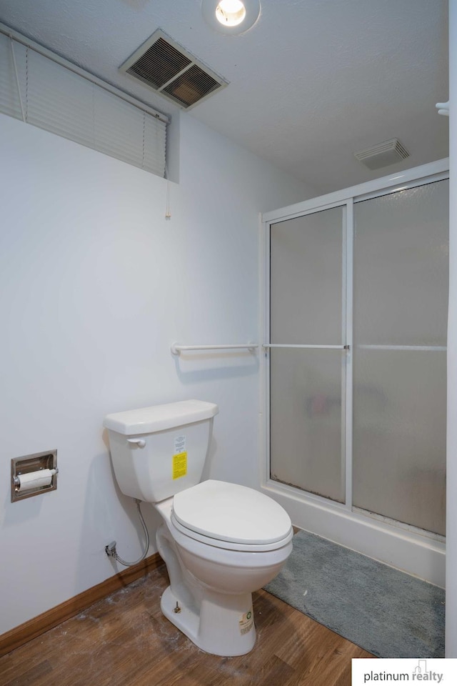 bathroom with toilet, a shower with shower door, and hardwood / wood-style floors