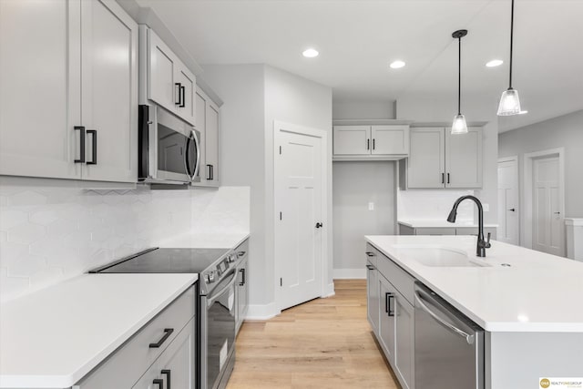 kitchen featuring pendant lighting, decorative backsplash, sink, a kitchen island with sink, and appliances with stainless steel finishes