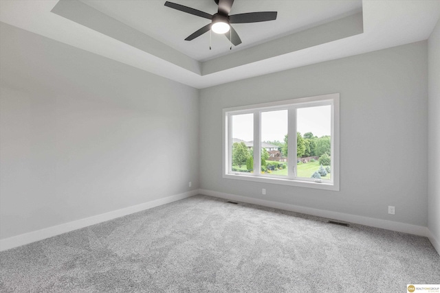 carpeted empty room with a raised ceiling and ceiling fan