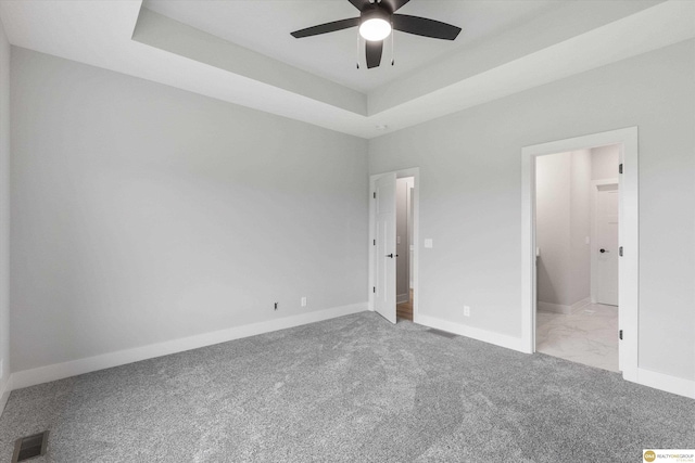 unfurnished bedroom with light colored carpet, ceiling fan, connected bathroom, and a raised ceiling