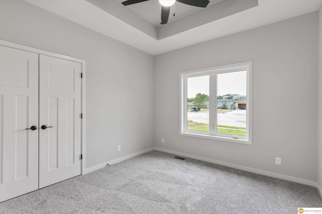 unfurnished room with a raised ceiling, light colored carpet, and ceiling fan