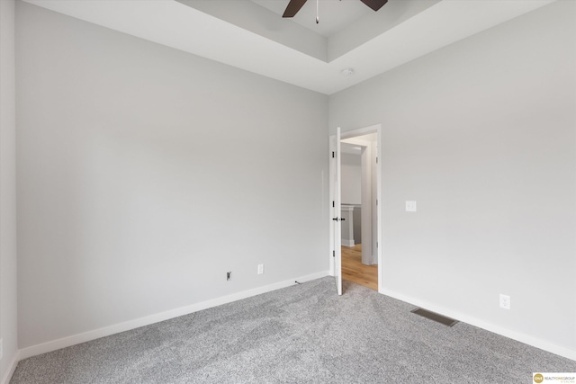 spare room with carpet floors, a tray ceiling, and ceiling fan