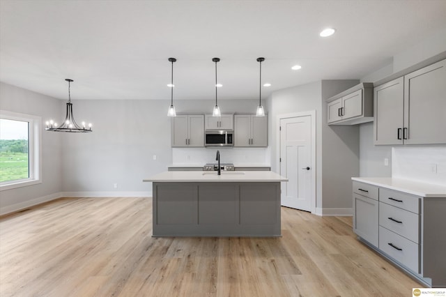 kitchen with an inviting chandelier, light hardwood / wood-style floors, gray cabinets, decorative light fixtures, and a kitchen island with sink