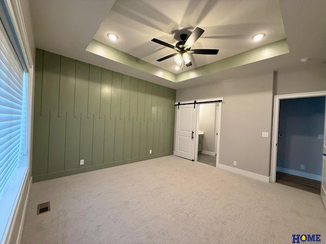 unfurnished bedroom featuring ceiling fan, light carpet, a raised ceiling, and a barn door