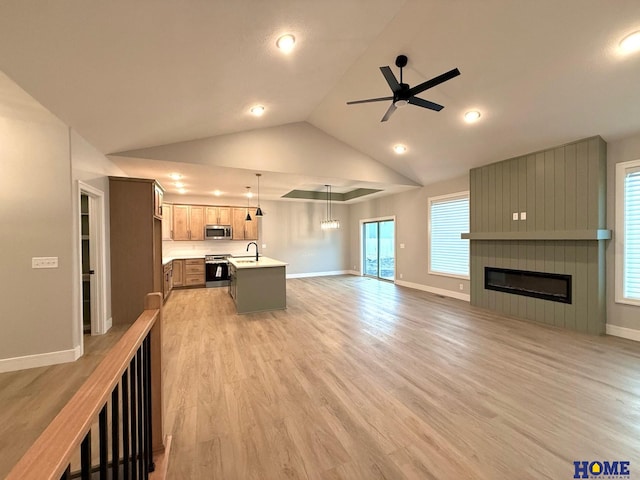 unfurnished living room with ceiling fan, light wood-type flooring, a fireplace, vaulted ceiling, and sink