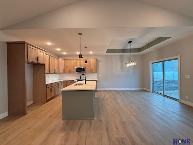 kitchen with light hardwood / wood-style floors, decorative backsplash, a kitchen island with sink, hanging light fixtures, and sink